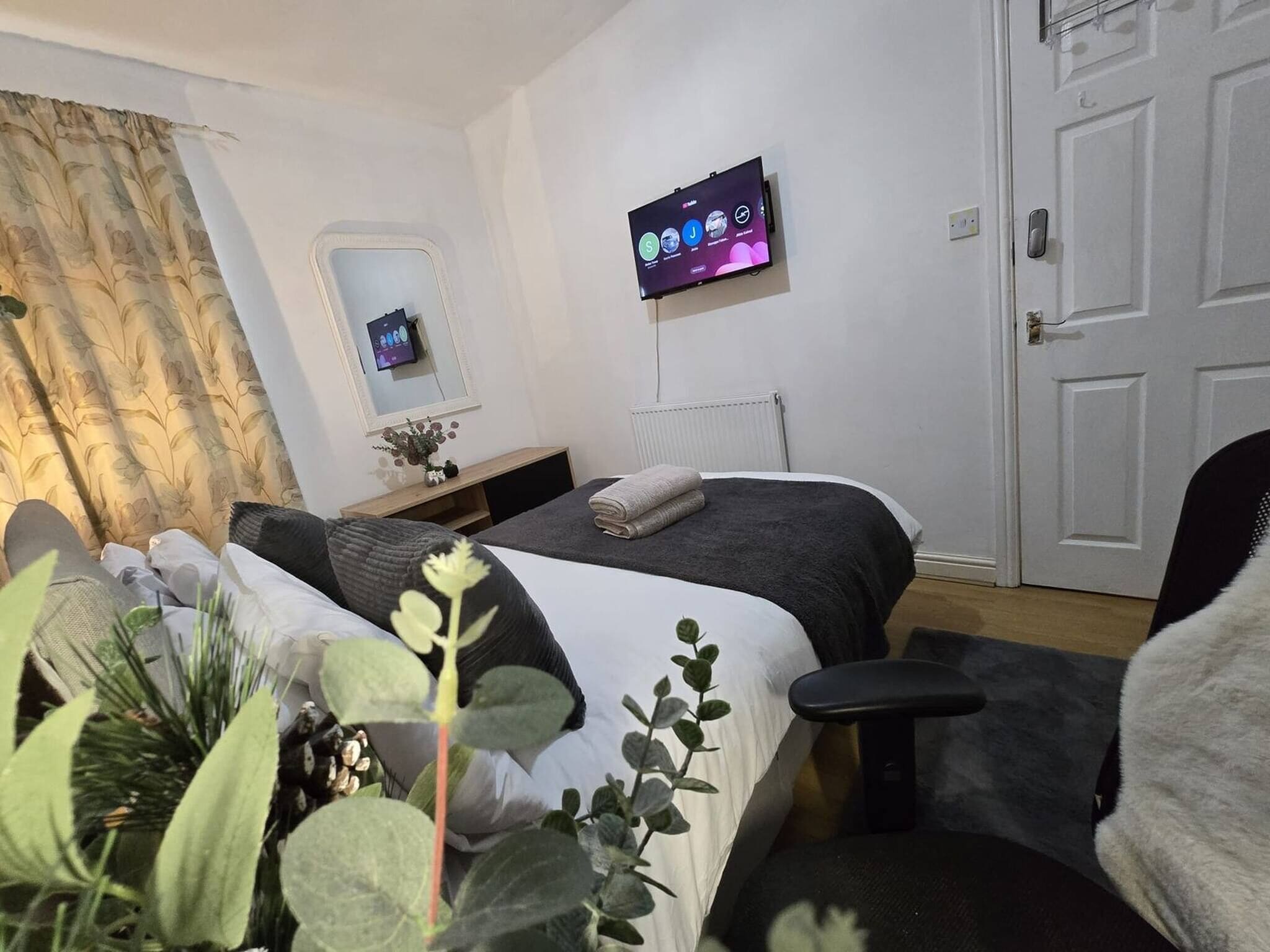 Een hotelkamer met een bed, een aan de muur bevestigde televisie, een nachtkastje met een lamp en een deur.