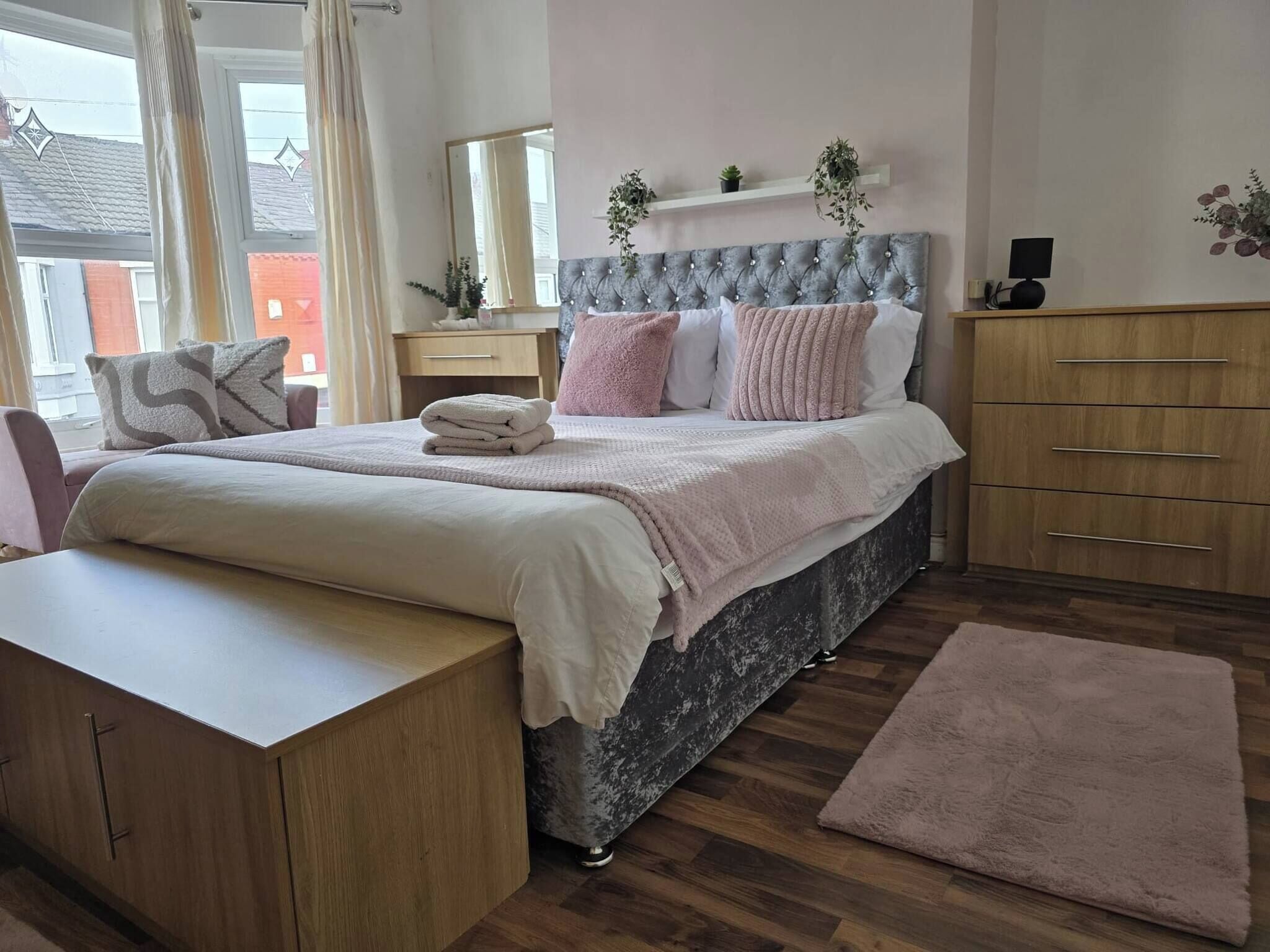 Un dormitorio con cama, mesitas de noche, cómoda, mesilla de noche y ventana con cortinas.
