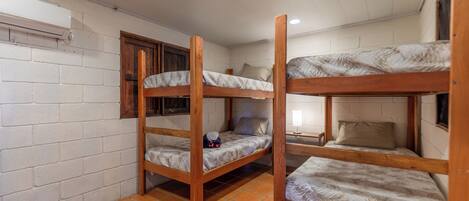 Une chambre de dortoir avec trois lits superposés, des murs en briques blanches et un sol carrelé.