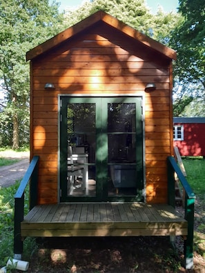 A wooden cabin with a porch, a sliding glass door, and a small outdoor seating area. - Cozy Tiny House in the Countryside (Nutteln)