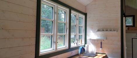A wooden cabin interior with a large window, a sink, and a shelf with cups.
