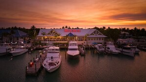 Ein Yachthafen mit mehreren angesterten Booten, ein Gebäude mit einer Beschilderung und ein Sonnenuntergang im Hintergrund.