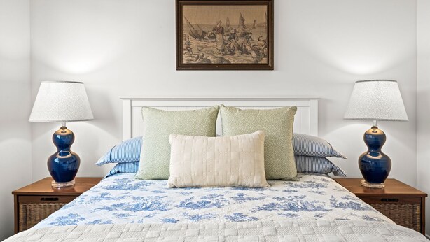 A neatly made bed with a floral-patterned bedspread, two matching nightstands with lamps, and a framed artwork above the bed. - Kenmare - A Curated Coastal Retreat (St Leonards)