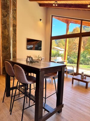 A dining area with a wooden table, two chairs, and a view of the outdoors through large windows.