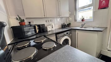 Een functionele keuken met een fornuis, magnetron, broodrooster en wasmachine.
