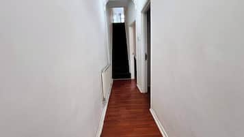 Passadís estret amb parets blanques i terres de fusta, que porta a una habitació fosca.
