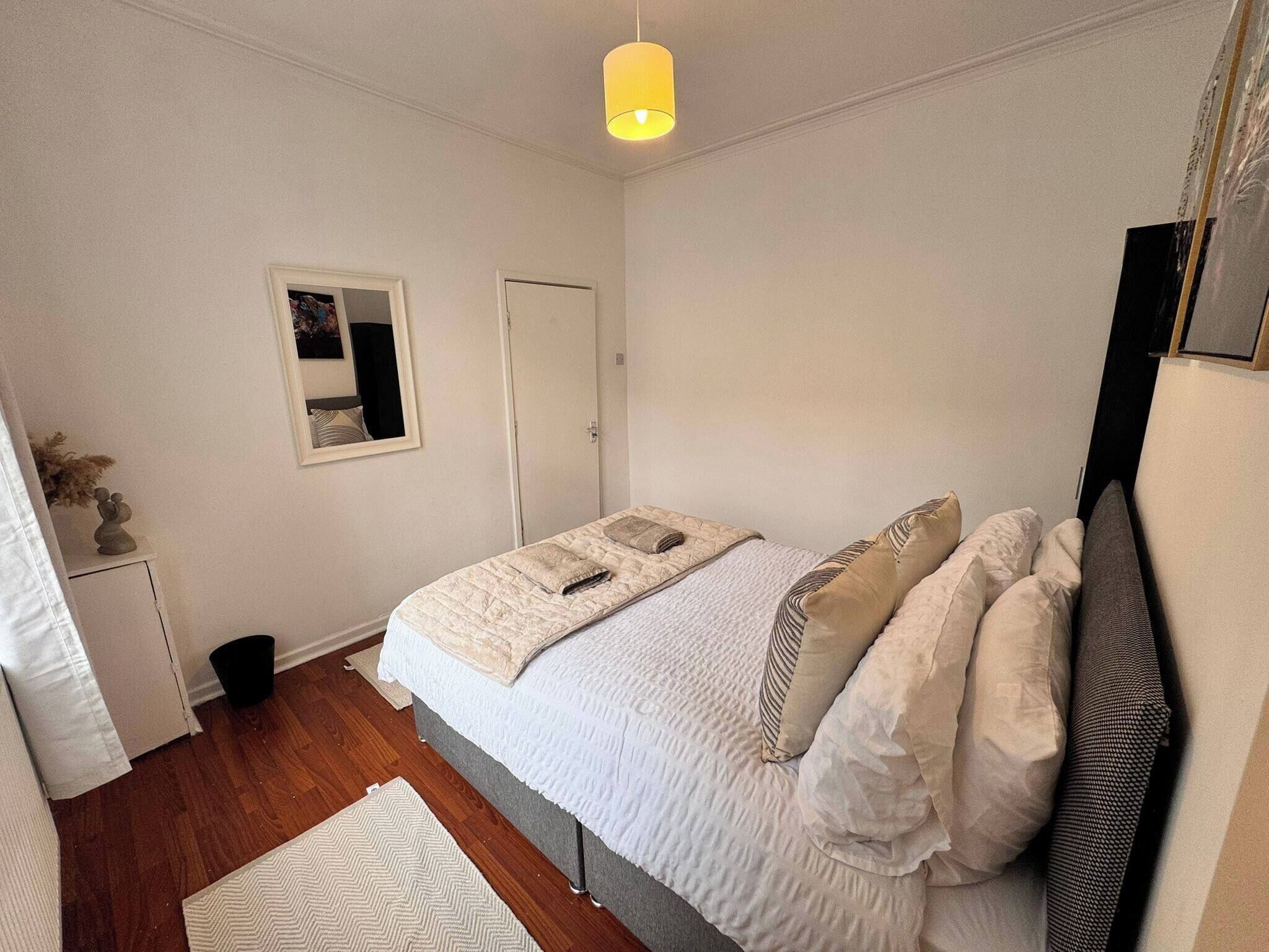 A bedroom with a bed, a bedside table, a lamp, a door, and a framed picture on the wall.