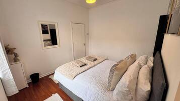 A bedroom with a bed, a bedside table, a lamp, a door, and a framed picture on the wall.