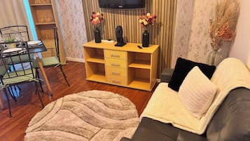 Un saló amb un sofà, una televisió, un moble de fusta i una zona de menjador amb cadires i una taula.