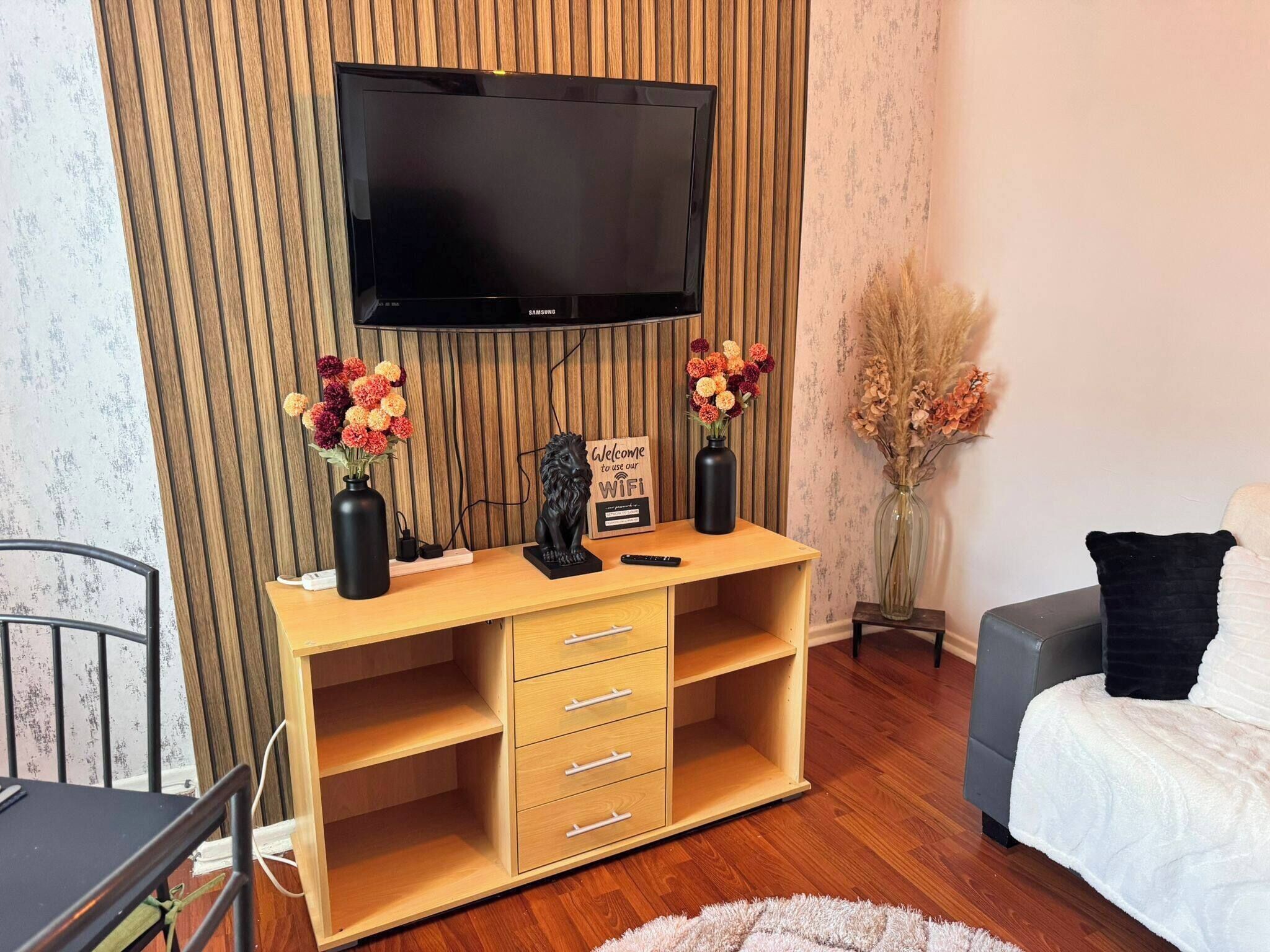 Ein Zimmer mit einem HolztV-Schrank, einem flachbildfernseher darüber und einem Bett mit weißer Bettdecke.