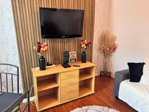 Ein Zimmer mit einem HolztV-Schrank, einem flachbildfernseher darüber und einem Bett mit weißer Bettdecke.
