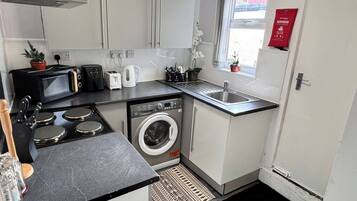 Een compacte keuken met een wasmachine, een magnetron, een broodrooster en een spoelbak.