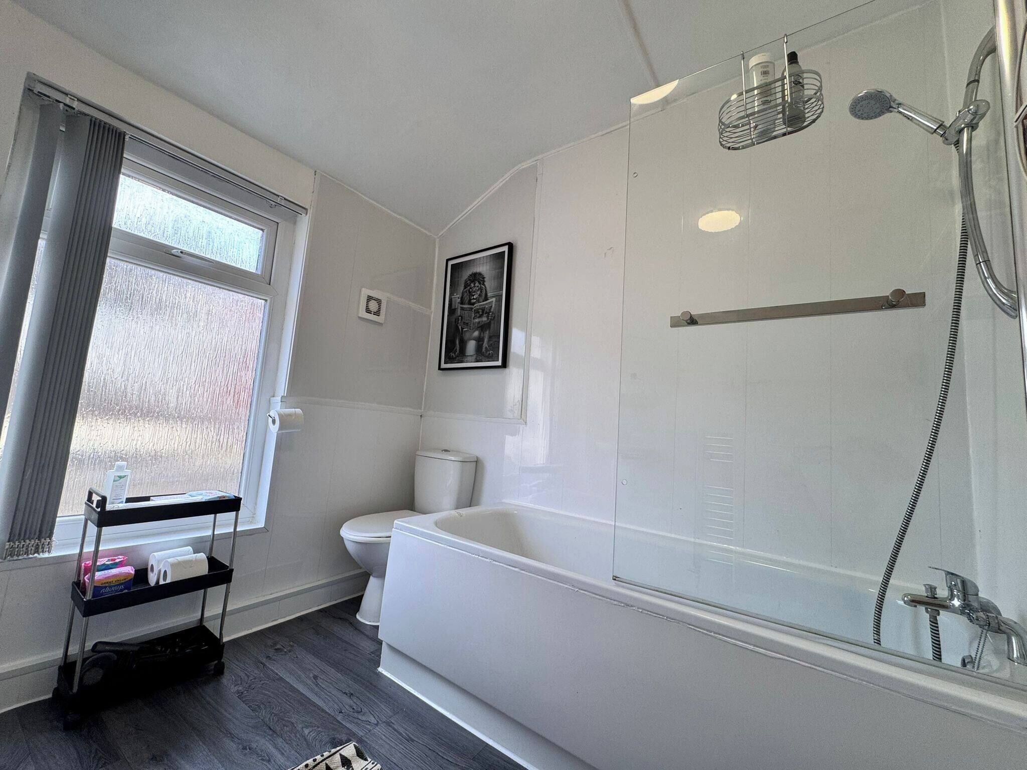 A modern bathroom with a bathtub, shower, toilet, and a window with a view.