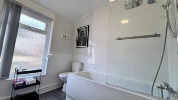 A modern bathroom with a bathtub, shower, toilet, and a window with a view.