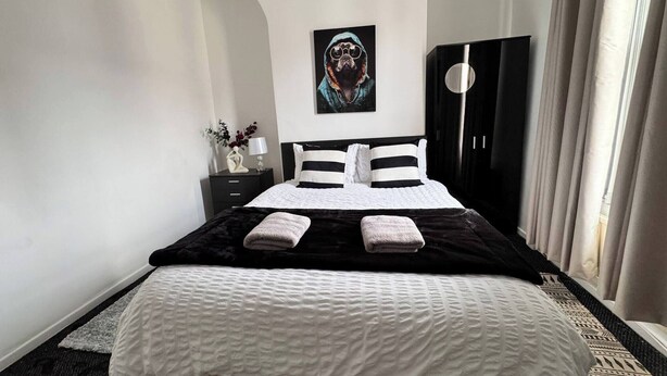 A hotel room with a bed, a nightstand, a lamp, a painting, and a wardrobe. - House 10 Minutes From the Center (Liverpool)
