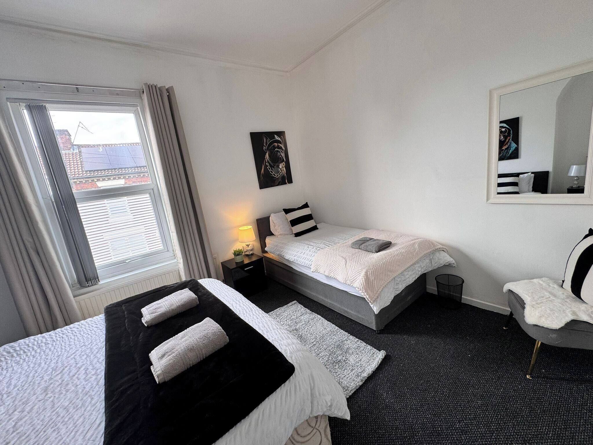 Una habitació d'hotel amb dos llits, una finestra amb cortines, una taula de nit amb una làmpada, un quadre penjat a la paret i un mirall.