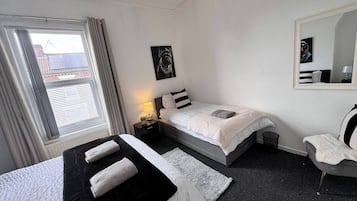 Una habitació d'hotel amb dos llits, una finestra amb cortines, una taula de nit amb una làmpada, un quadre penjat a la paret i un mirall.