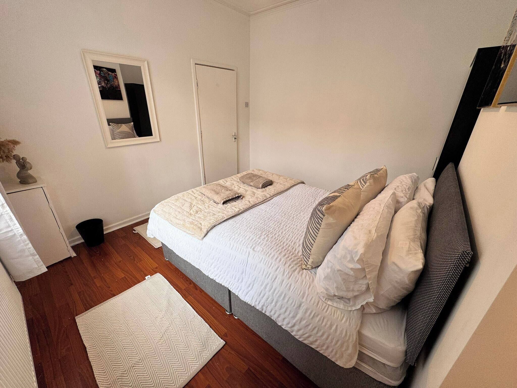 A bedroom with a bed, a bedside table, a mirror, a door, and a small rug.