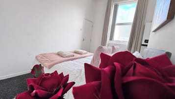 A hotel room with a bed, a window with curtains, and a large red rose in the foreground.