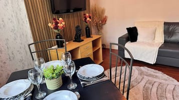 Een eettafel gedekt met borden, glazen en bestek, een kamerplant en een aan de muur bevestigde televisie.