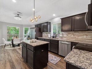 A modern kitchen with dark cabinetry, a granite countertop, and a built-in dishwasher. - Tranquil 3-bedroom house in charming McKinney (McKinney)