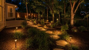 Ein angelegter Garten mit einem Steinweg, Bäumen und Außenbeleuchtung.