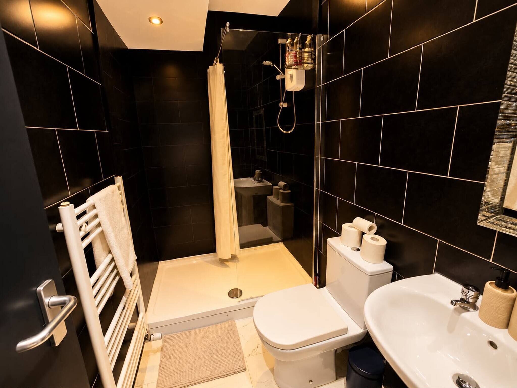 Un baño moderno con ducha, inodoro y lavamanos, con azulejos negros y un perchero blanco.