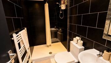 A modern bathroom with a shower, toilet, and sink, featuring black tiles and a white towel rack.
