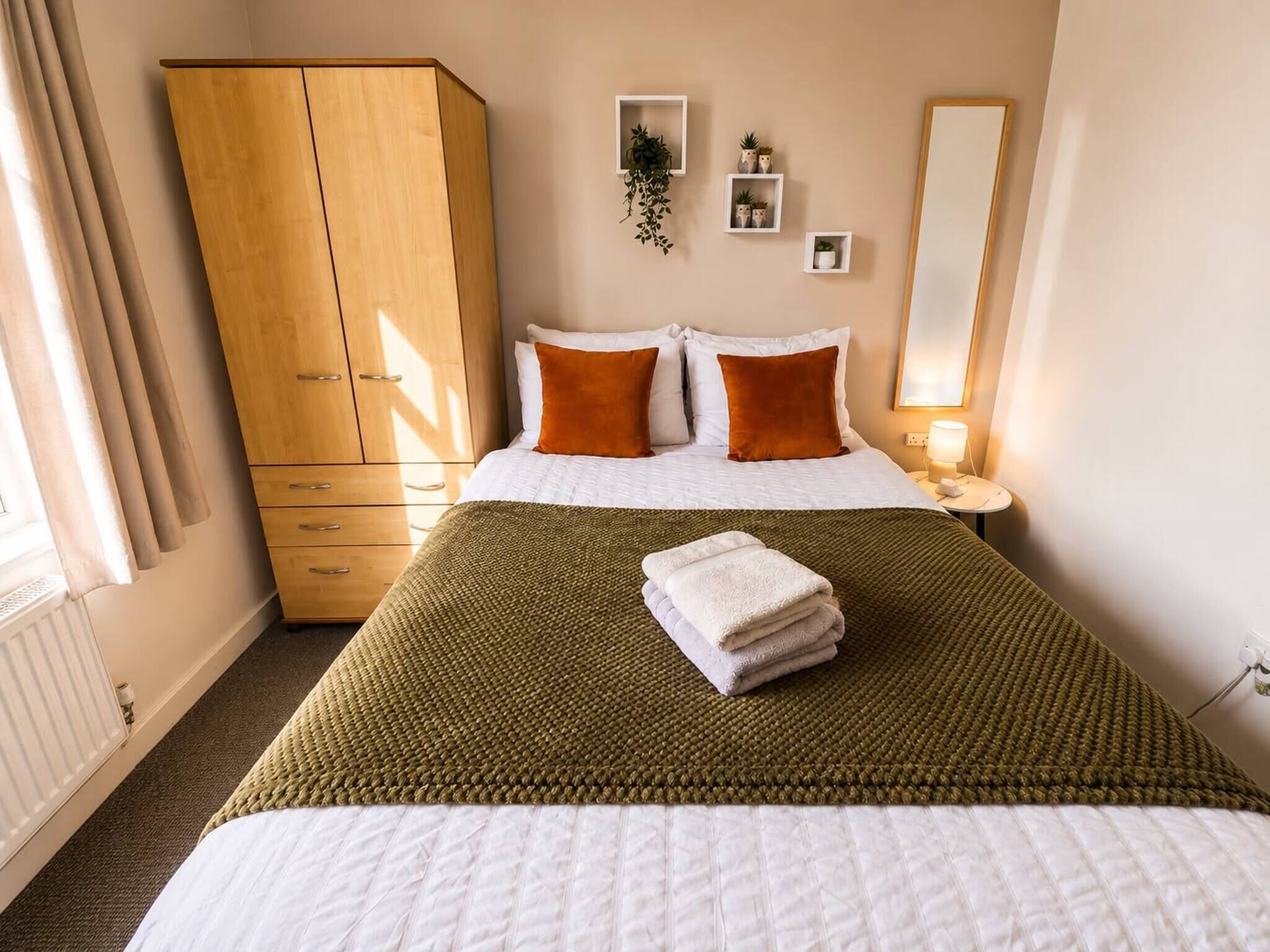 Une chambre d’hôtel comprenant un lit, une armoire, une table de chevet avec une lampe et un miroir fixé au mur.