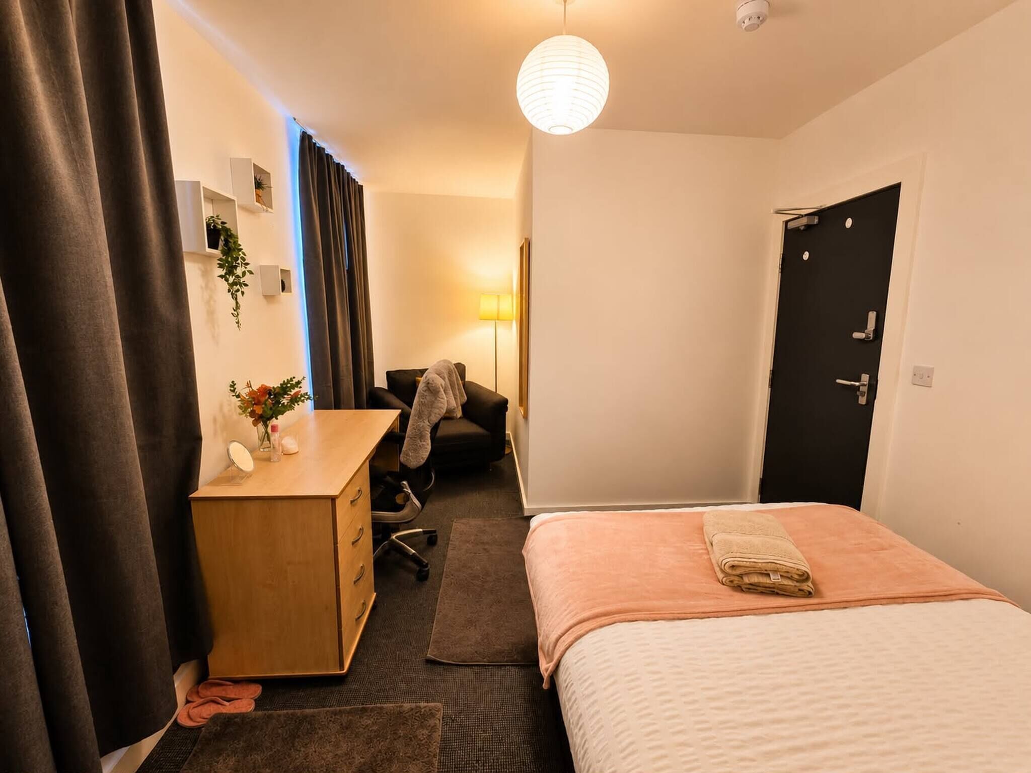 Ein Hotelzimmer mit Bett, Schreibtisch, Stuhl, Lampe und Tür.