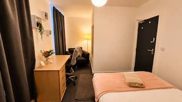 Ein Hotelzimmer mit Bett, Schreibtisch, Stuhl, Lampe und Tür.