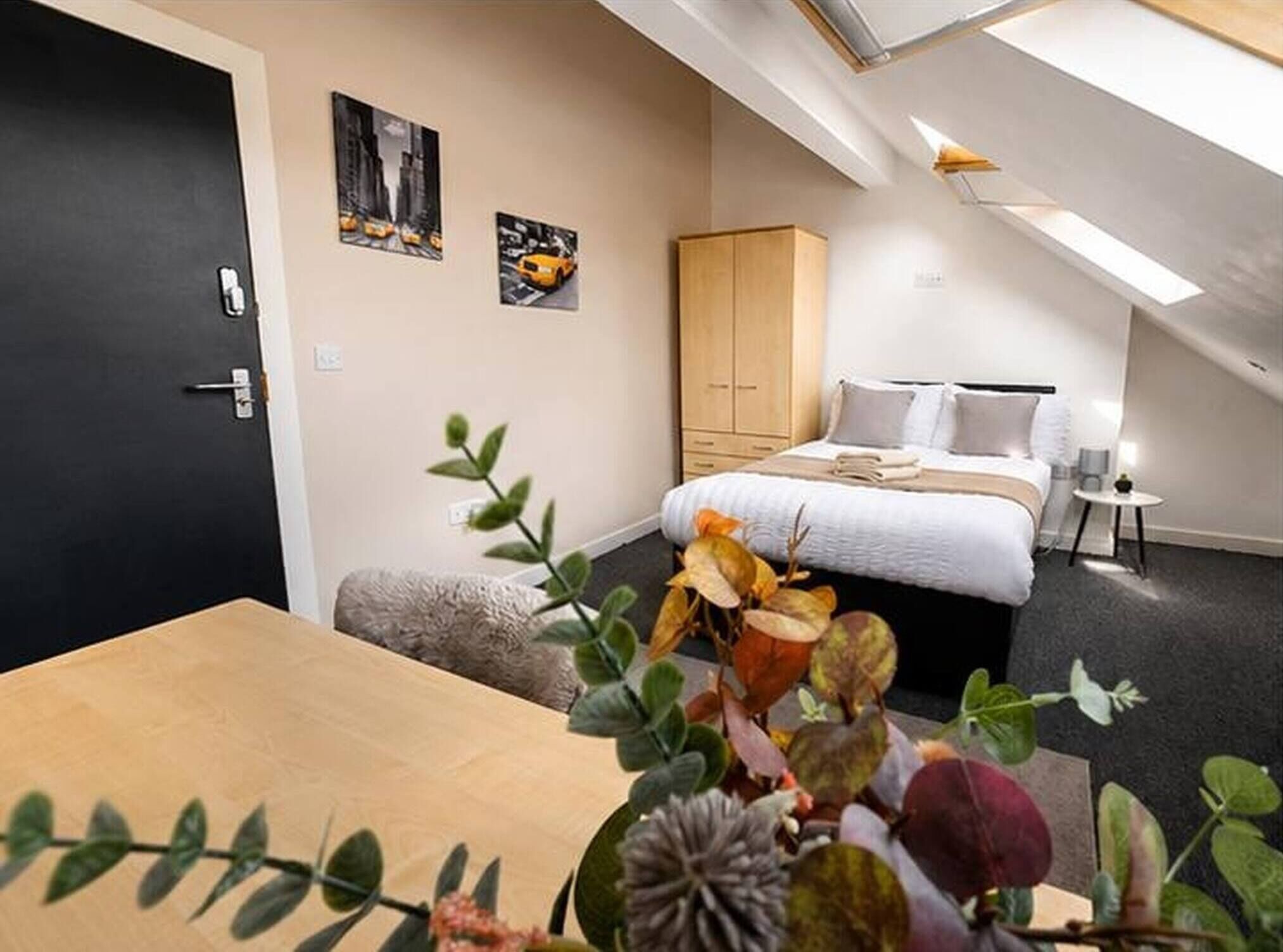A modern bedroom with a bed, a wooden wardrobe, a small table, and a plant.