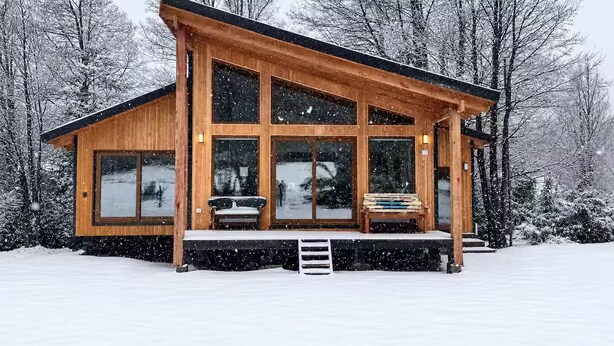 A wooden cabin with large windows, a porch, and a snow-covered landscape. - Casa para 8 Personas a solo 5 km de Corralco (Malalcahuello)