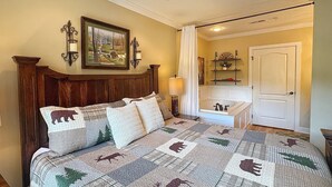 A bedroom with a wooden headboard, a bed with a quilt featuring animal prints, a nightstand with a lamp, a painting on the wall, and a door leading to another room. - Downtown Gatlinburg-Bear View Manor-Update - Renovated-near Convention Center (Gatlinburg)
