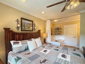 A bedroom with a wooden headboard, a bed with a quilt featuring animal prints, a nightstand with a lamp, a painting on the wall, and a door leading to another room. - Downtown Gatlinburg-Bear View Manor-Update - Renovated-near Convention Center (Gatlinburg)