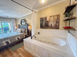 A bedroom with a large bed, a bathtub, a painting, and a balcony with a view. - Downtown Gatlinburg-Bear View Manor-Update - Renovated-near Convention Center (Gatlinburg)