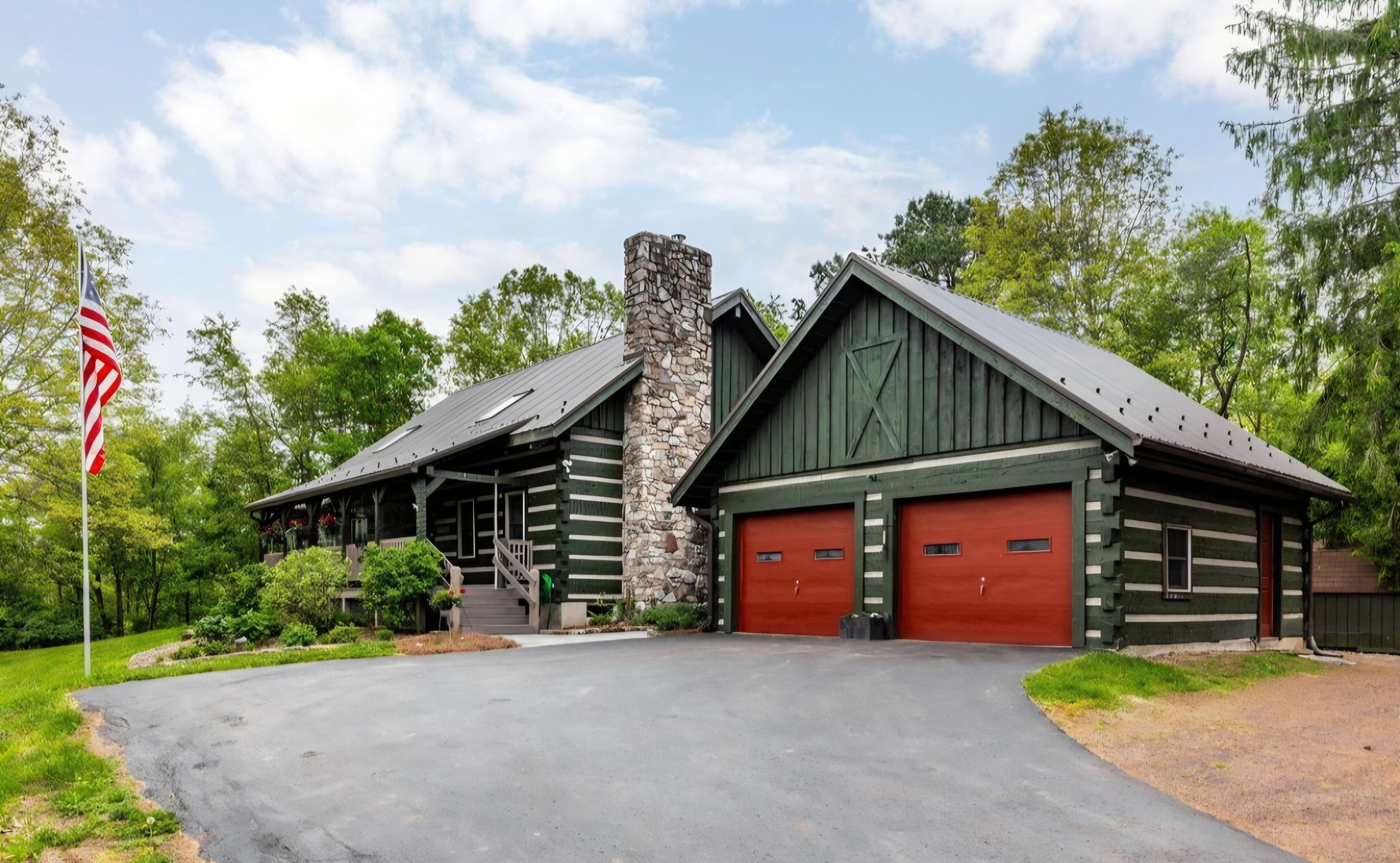 A log cabin with a stone chimney, two red garage doors, and a flagpole with an American flag.