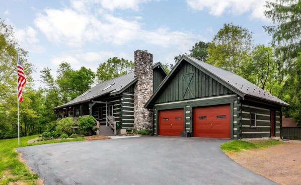 A log cabin with a stone chimney, two red garage doors, and a flagpole with an American flag.