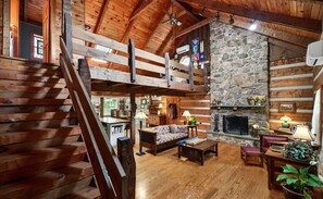 A log cabin interior with a stone fireplace, wooden staircase, and a cozy seating area. - Fabulous 4-bed/bath log home w/ HVAC private walking trail& Theater in Lewisburg (Lewisburg)
