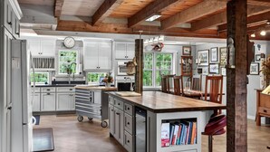 Una cocina amplia con gabinetes blancos, techo de madera y una isla grande con estantería empotrada.
