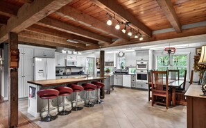 A spacious kitchen with white cabinets, a wooden island with bar stools, and a dining area with a chandelier.