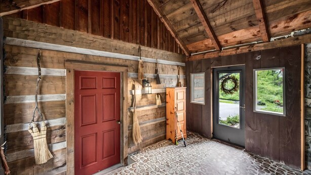 Un interior rústico de madera con una puerta roja, un armario de madera y una ventana adornada con un adorno.