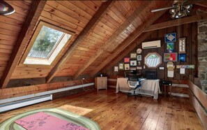 A cozy attic room with wooden beams, a skylight, a desk with a chair, and various framed pictures on the walls.