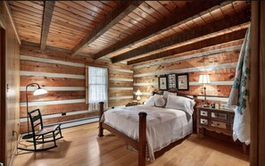 A wooden cabin-style bedroom with a bed, rocking chair, bedside tables, and a window.