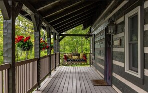 A covered porch with a wooden bench and a hanging flower basket.