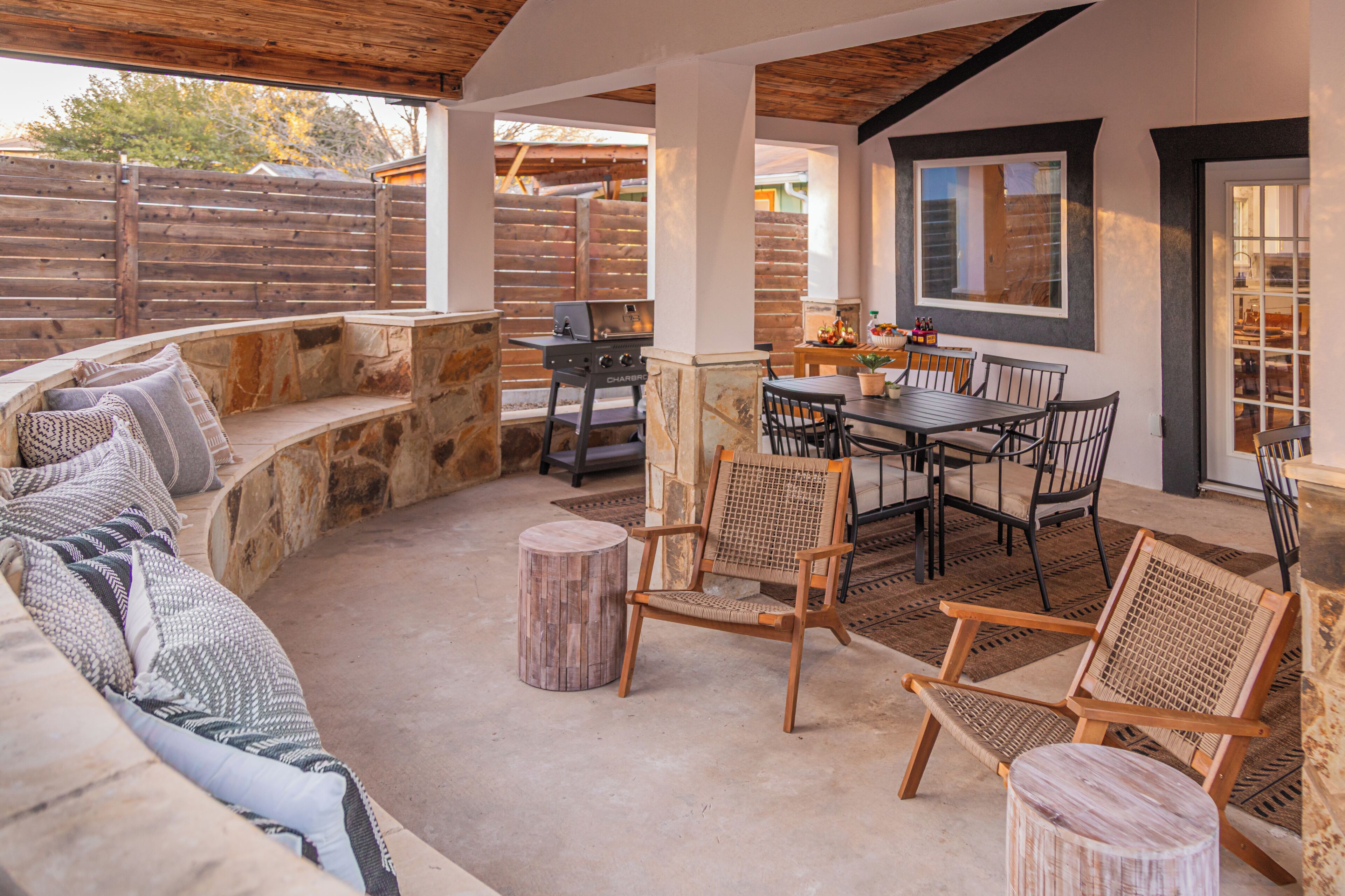 Un patio exterior con un banco de piedra, una parrilla, una mesa de comedor con sillas y un techo de madera.