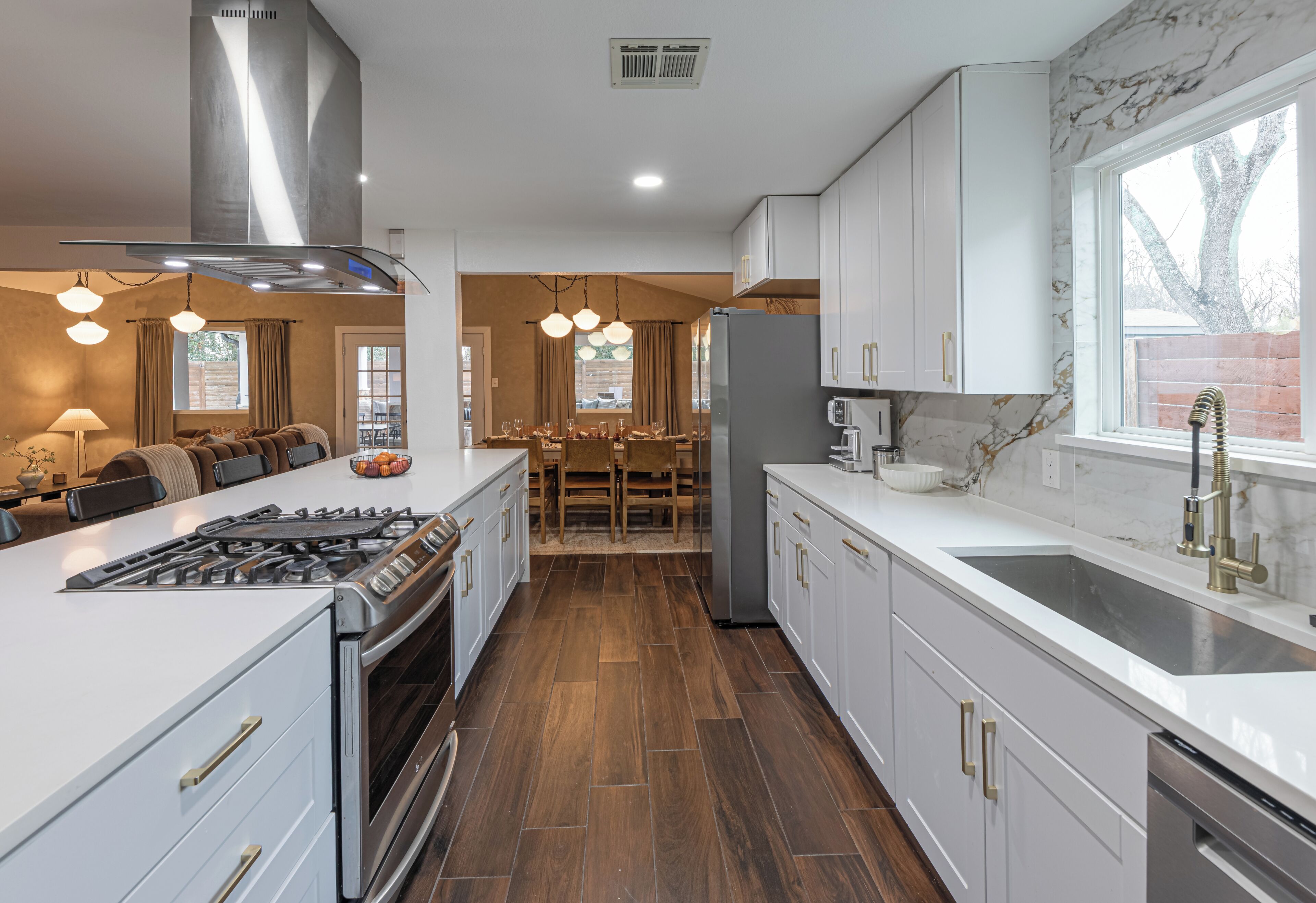 A modern kitchen with white cabinetry, a stainless steel range hood, and a central island with seating.