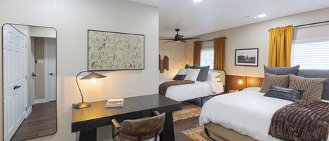 A hotel room with a bed, a desk with a chair, a ceiling fan, and a window with curtains.