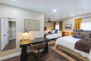 A hotel room with a bed, a desk with a chair, a ceiling fan, and a window with curtains. - Modern Cowboy Retreat, Outdoor Oasis, Billiards (Austin)