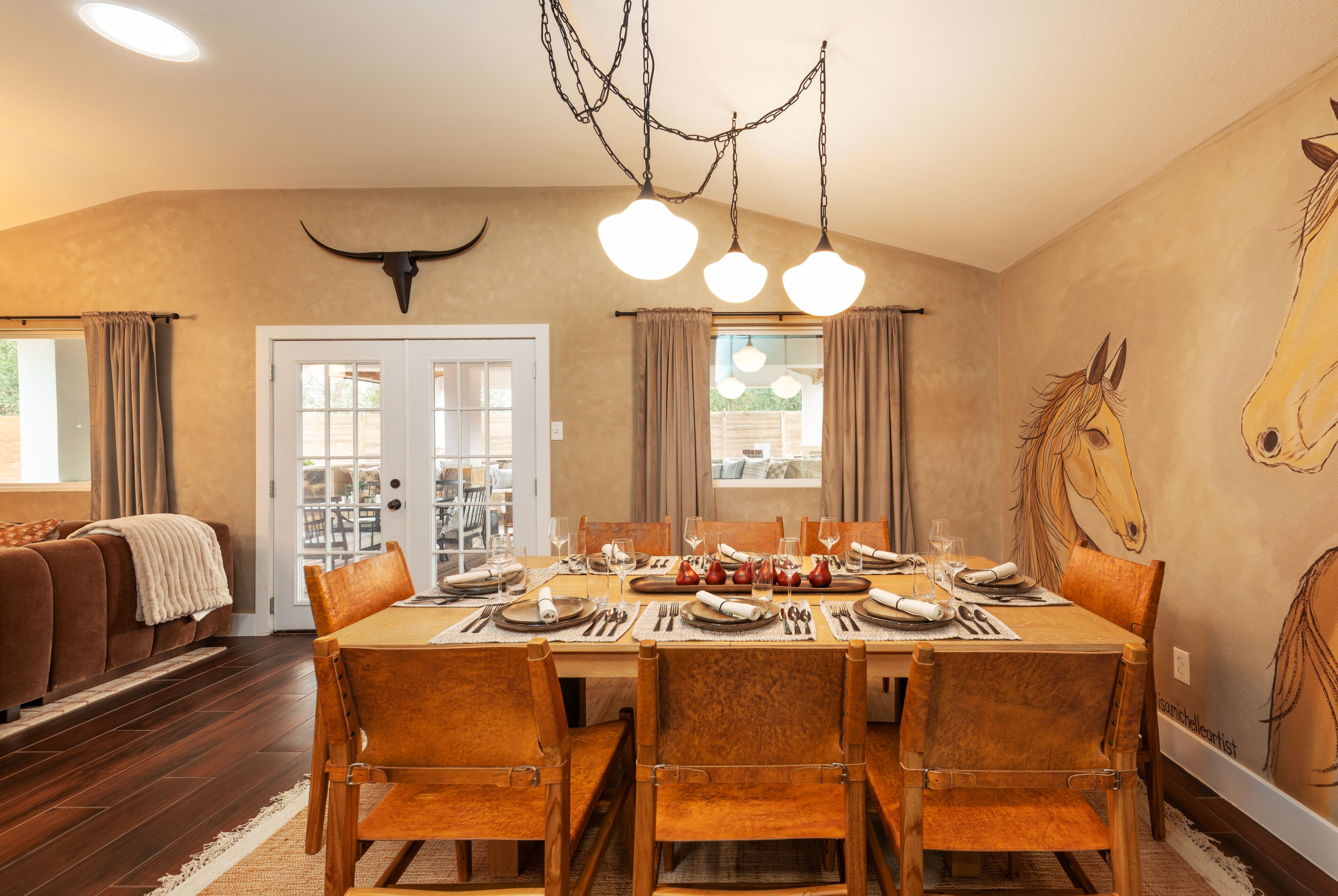 A dining room with a long table set for six, wooden chairs, and a chandelier.